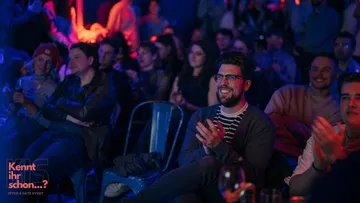 People sitting and clapping at indoor event.