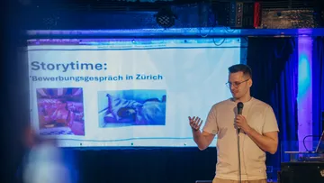 Man speaking on stage with presentation screen.