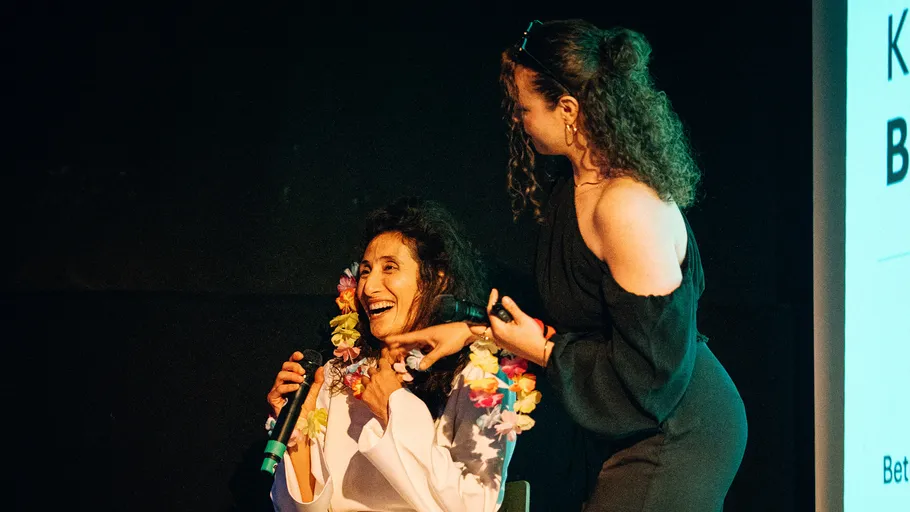 Two women on stage, one seated, smiling.