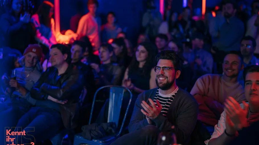 Audience sitting and clapping in a dimly lit room.