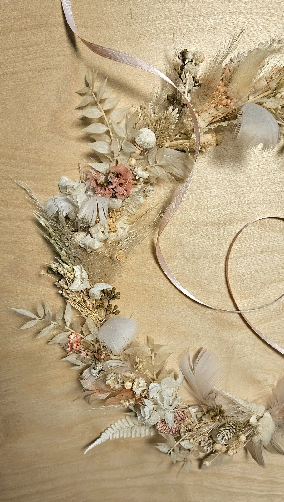 Dried floral wreath with ribbon on wooden surface.