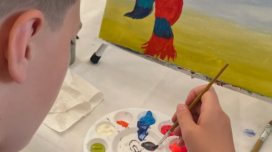 Person painting parrot on easel indoors.