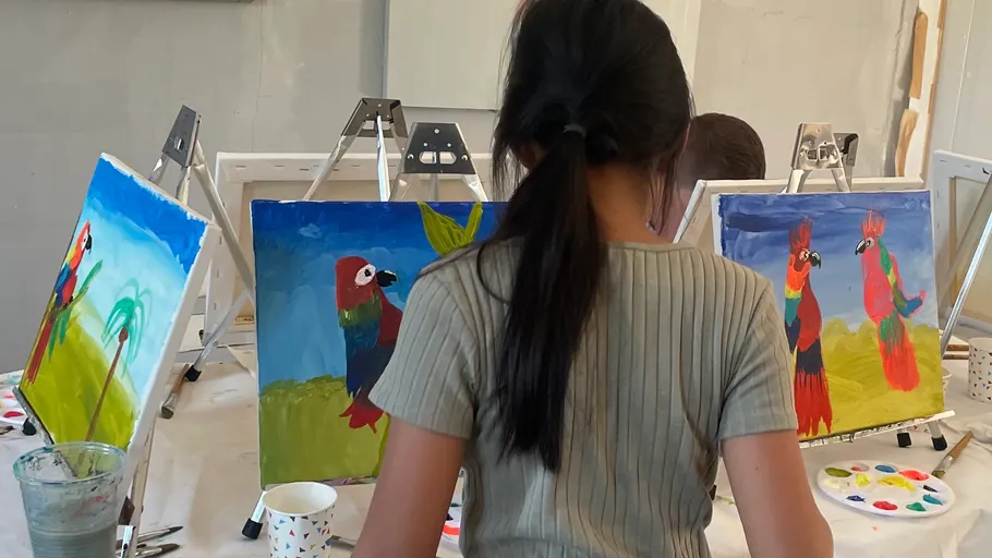Children painting parrots on canvases in a studio.
