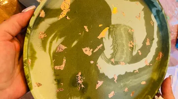 Green ceramic plate with gold flakes, held by hands.