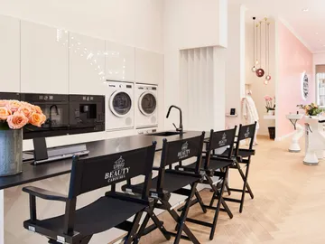 Modern kitchen with chairs, flowers and washing machines in the background.
