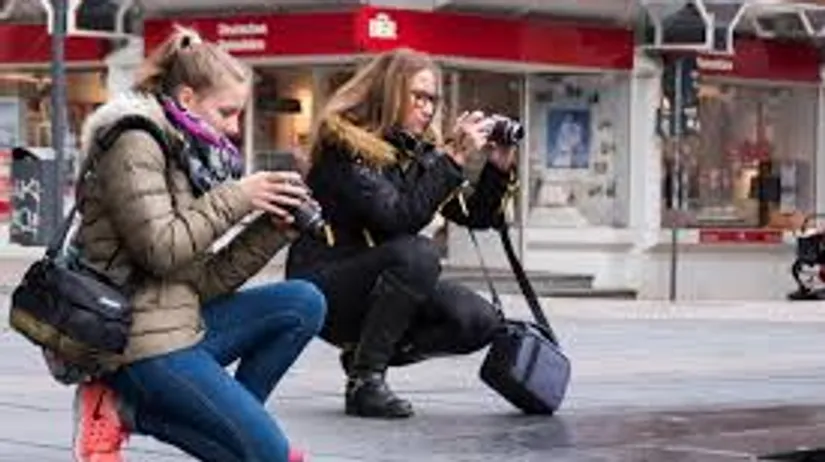 Two women crouching, photographing city scene.