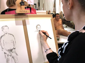 An artist draws a naked model in a studio.