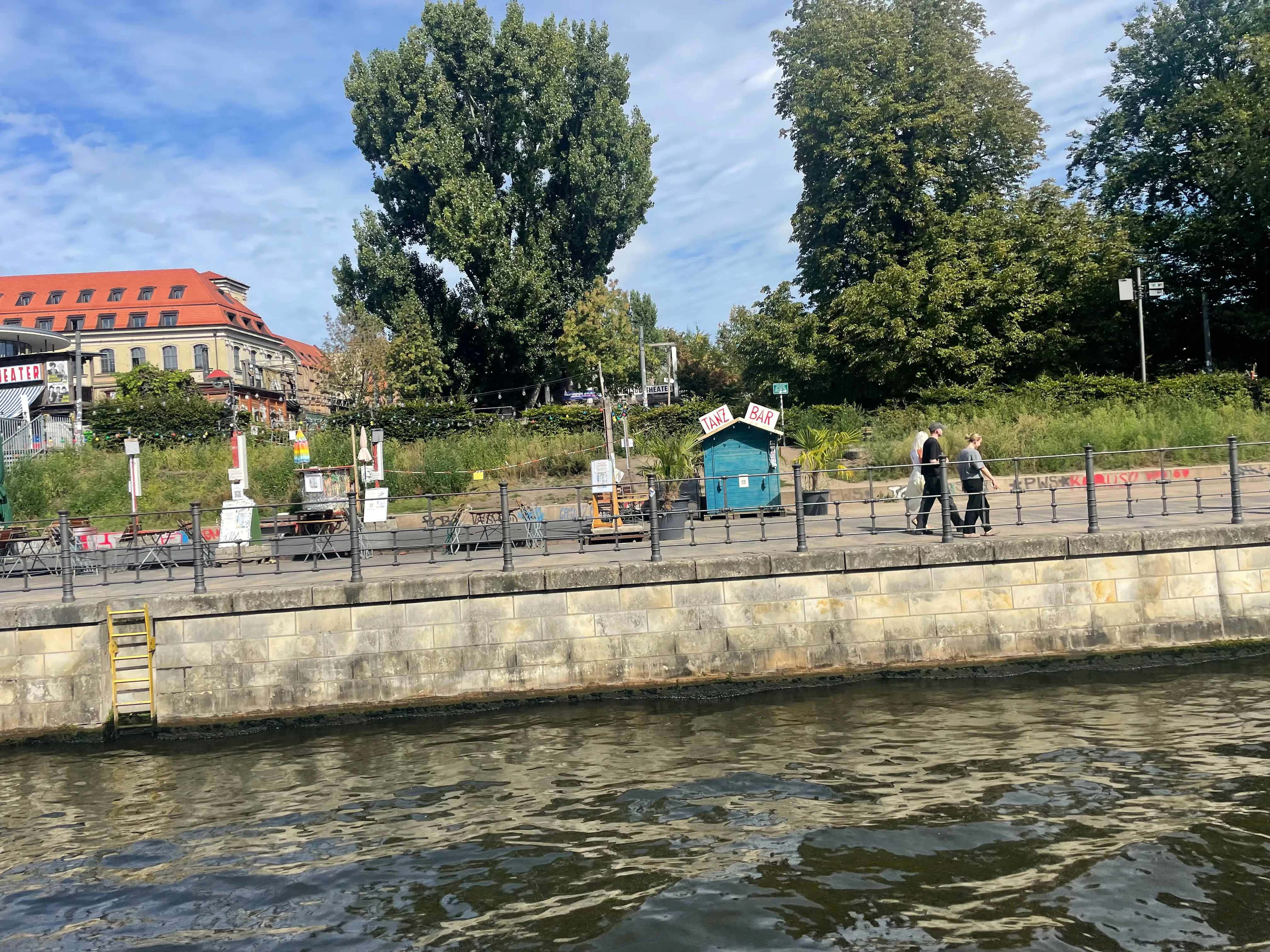 People walking along riverside with greenery