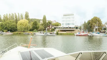 Flussblick mit Booten und modernem Gebäude.