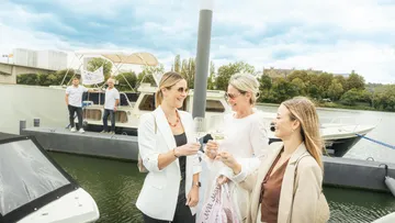 Three women toasting with wine on docked boat.