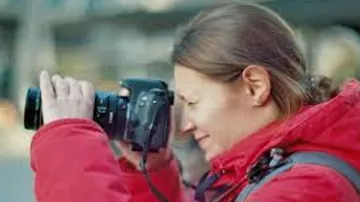 Person in red jacket taking photograph outdoors.
