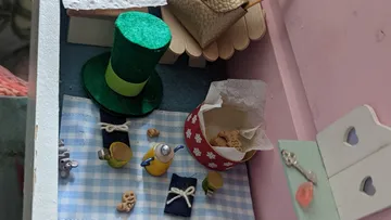 Miniaturszene mit Hut, Tassen, Snacks und Korb.
