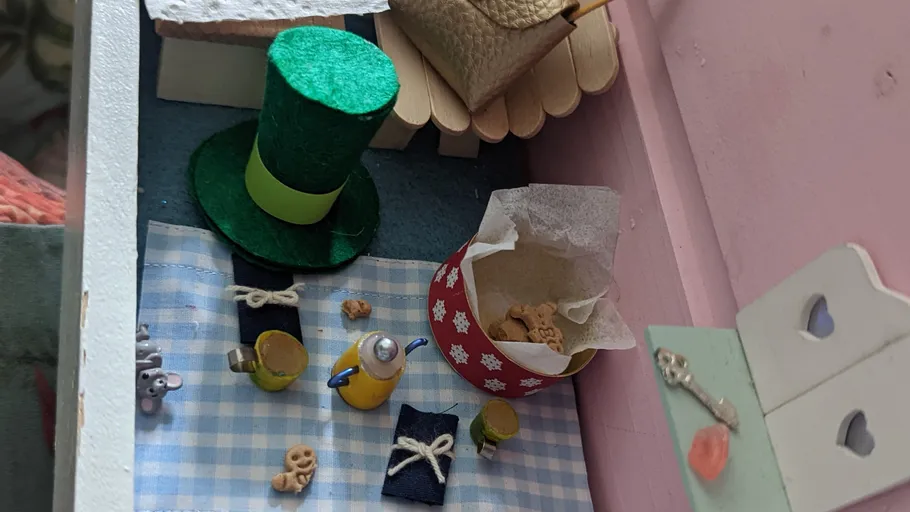 Miniaturszene mit Hut, Tassen, Snacks und Korb.