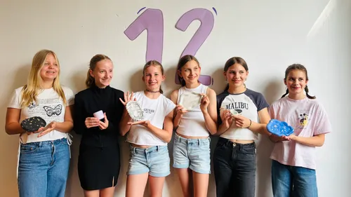 Six girls holding art objects, smiling indoors.