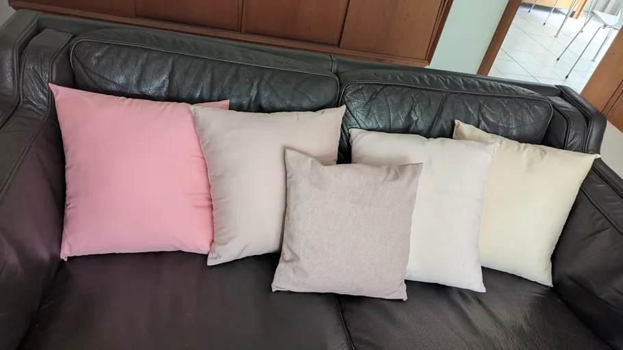 Fünf Kissen auf einem dunklen Ledersofa.