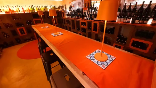 Langer Tisch mit orangen Lampen, umgeben von Weinflaschen.