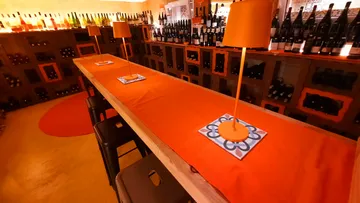 Long table with orange lamps and wine bottles.
