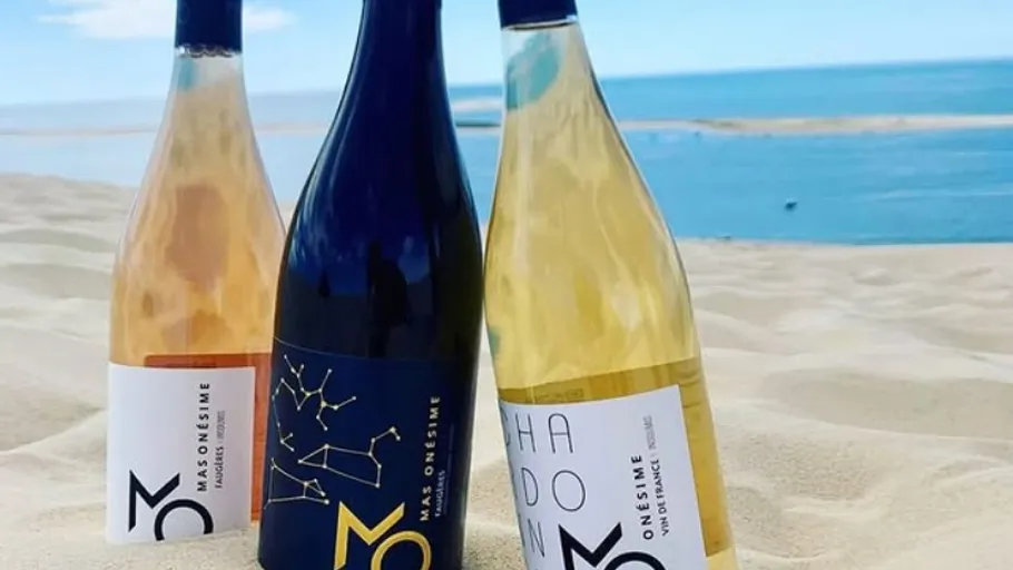 Three wine bottles standing on sandy beach.
