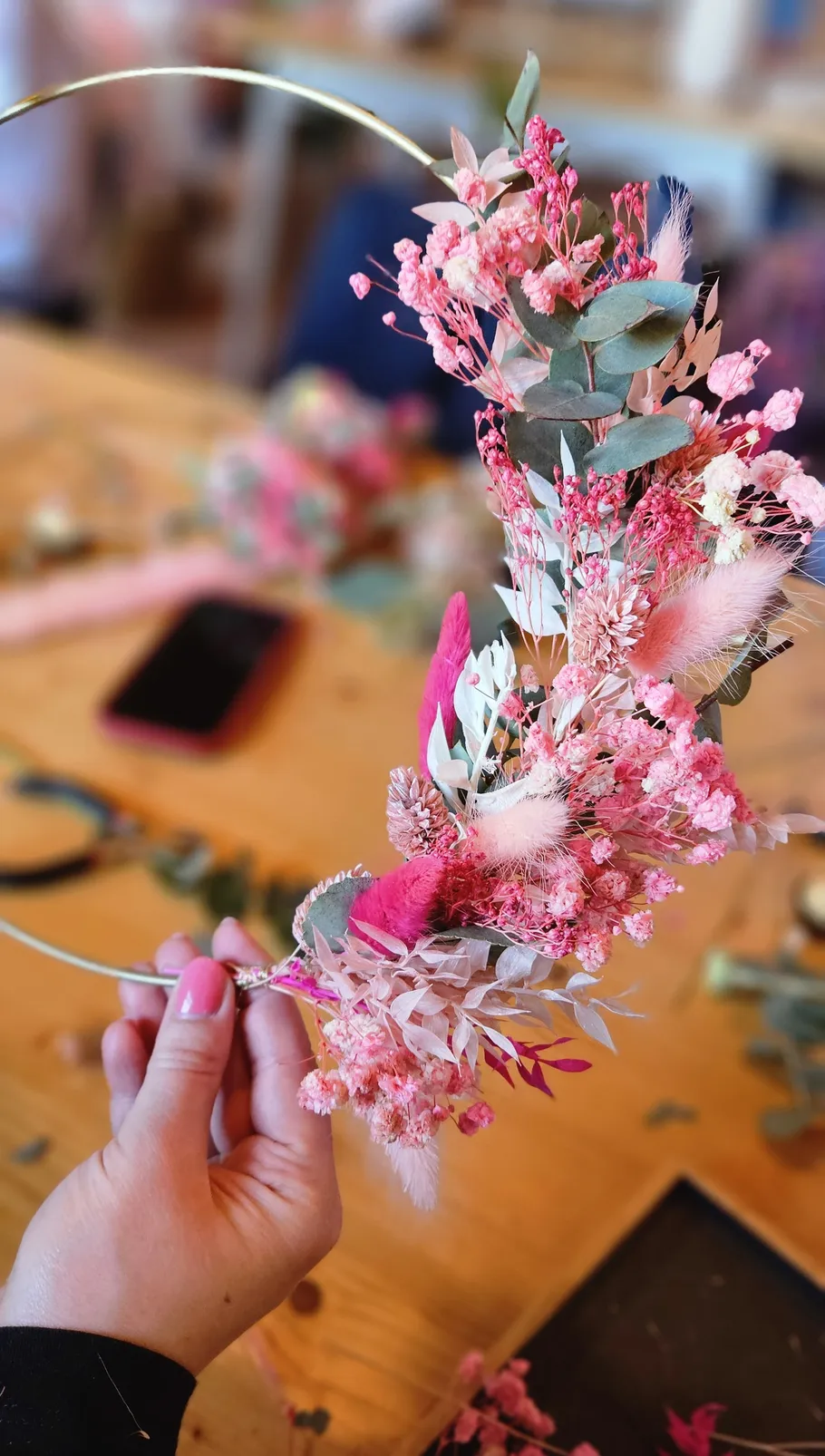 Hand hält Blumenringkranz, Holztisch im Hintergrund.