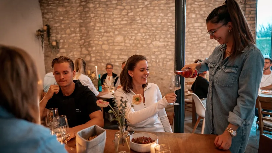 Person serviert Wein einer sitzenden Frau im Restaurant.