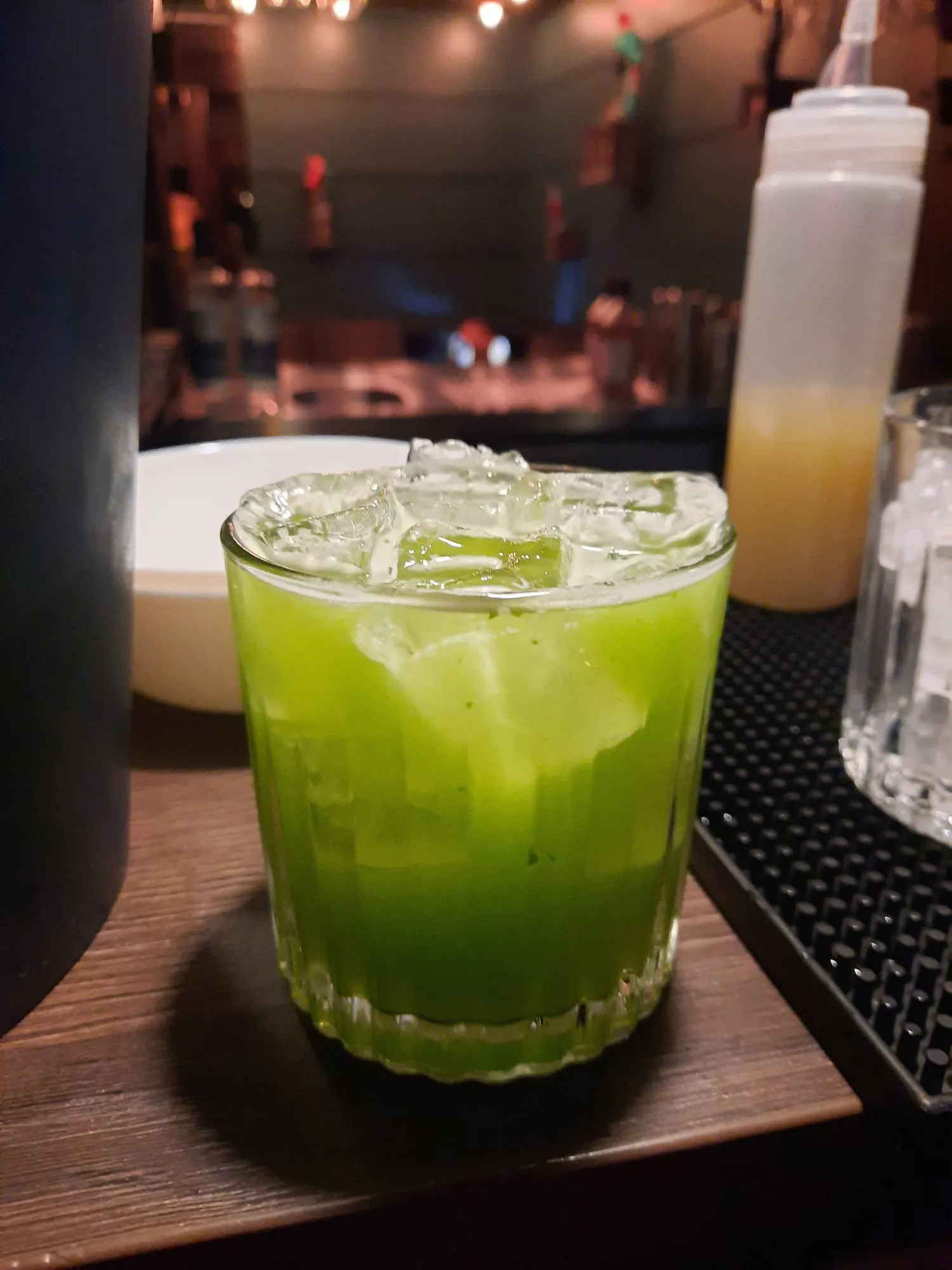 Grüner Cocktail mit Eiswürfeln auf Bartresen.