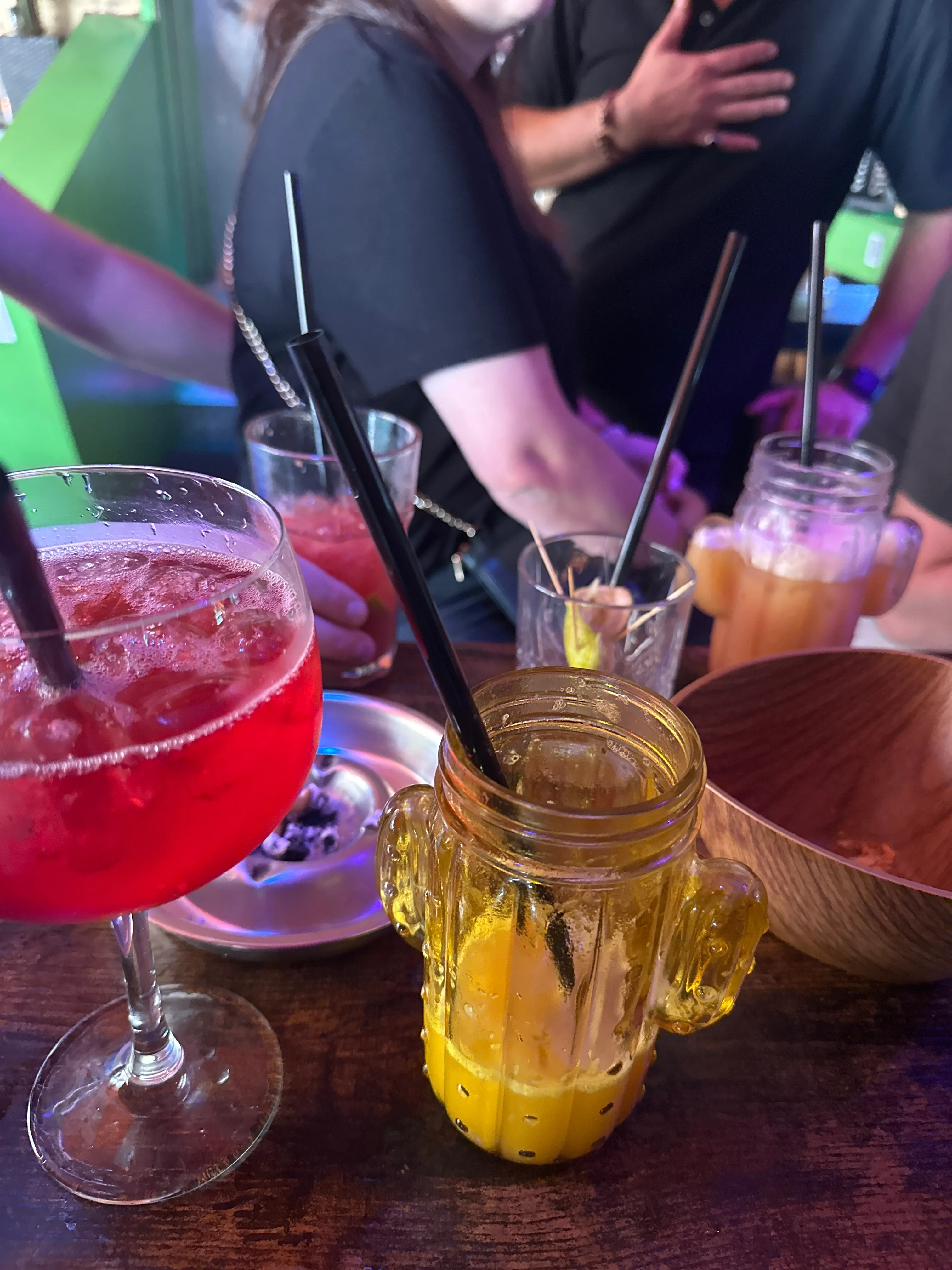 Colorful drinks on table with people nearby.