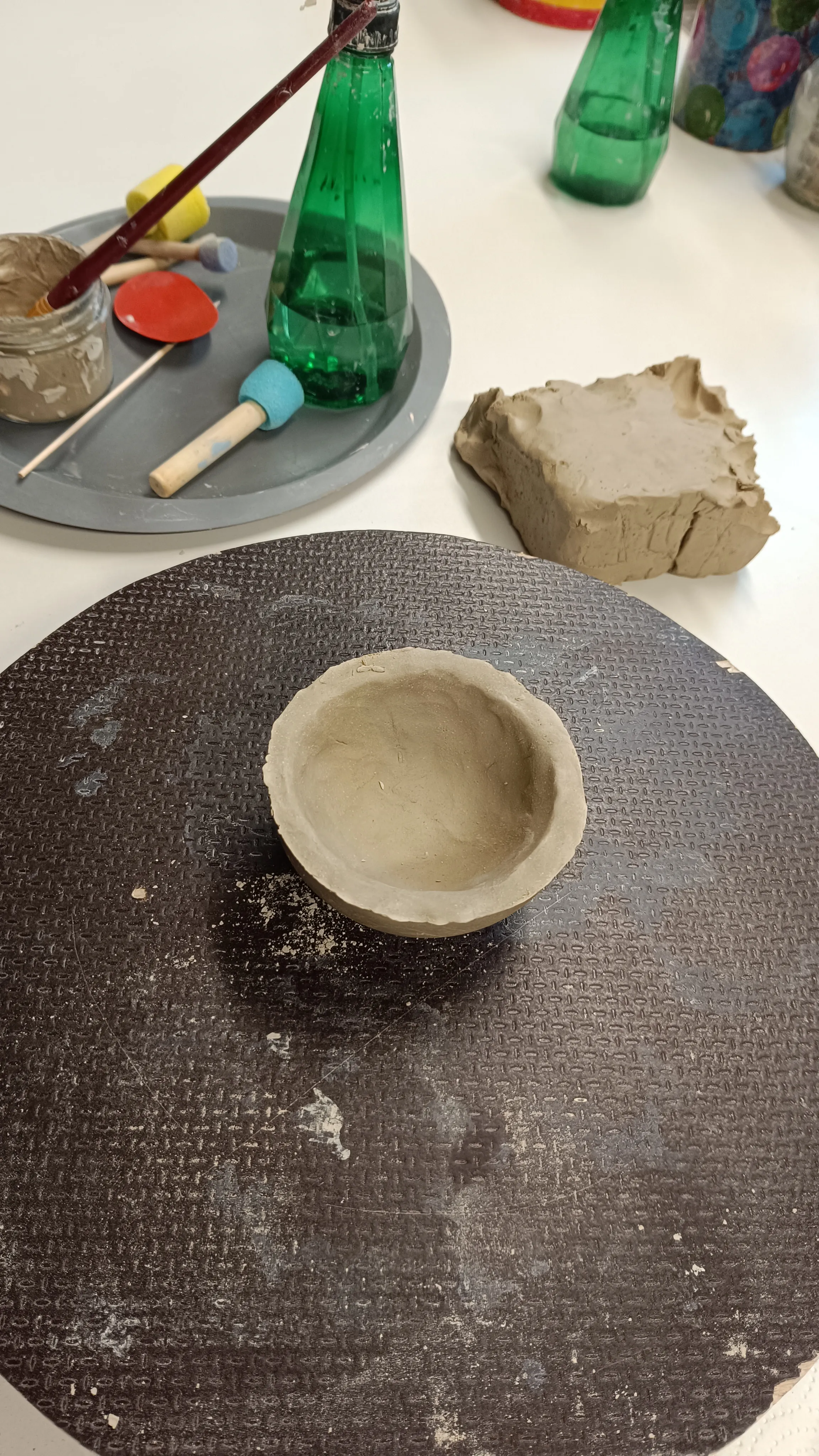 Clay bowl on pottery wheel with tools nearby.