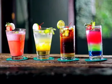 Vier bunte Cocktails stehen auf einem Holztisch.
