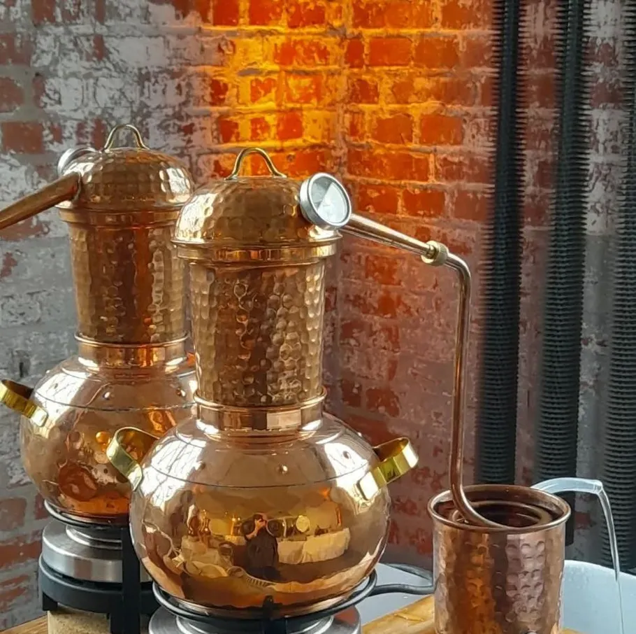 Copper stills on a wooden table, brick wall background.