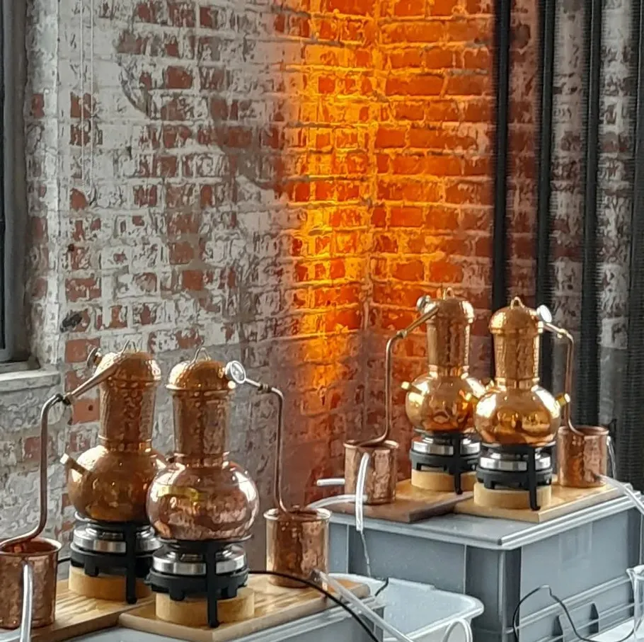Copper stills on tables against brick wall.