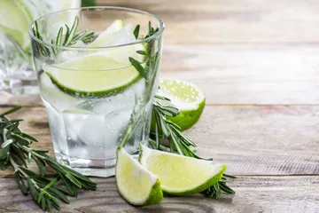 Glas mit Limette und Rosmarin auf Tisch.