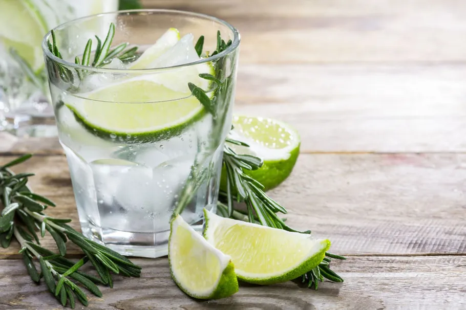 Glas mit Limette und Rosmarin auf Tisch.