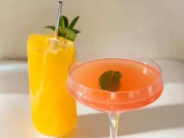 Zwei Cocktails stehen auf einem Tisch, einer orange, einer rosa.
