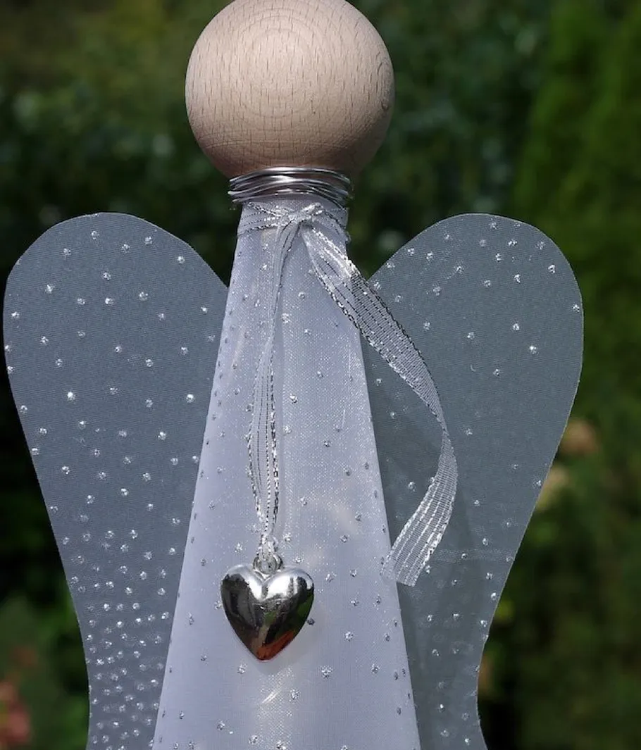 Wooden angel figure with heart pendant outdoors.