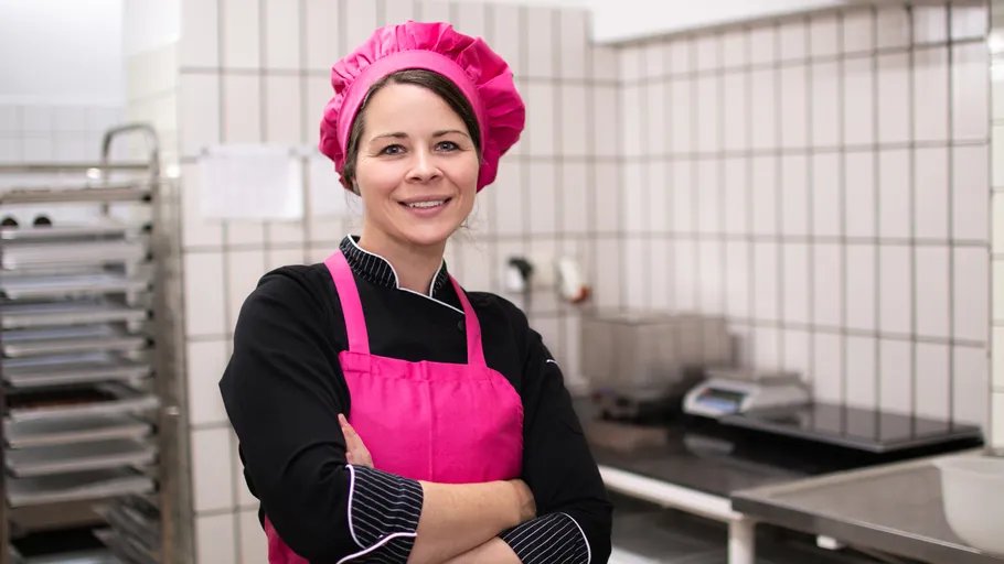Koch in pinker Uniform lächelt in Küche.