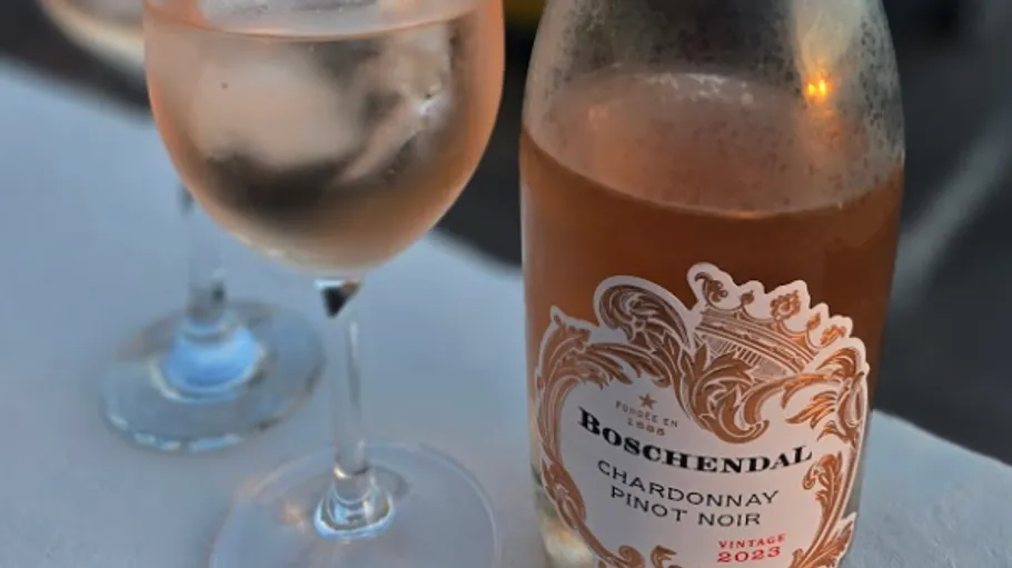 Rosé wine bottle beside filled glass outdoors.