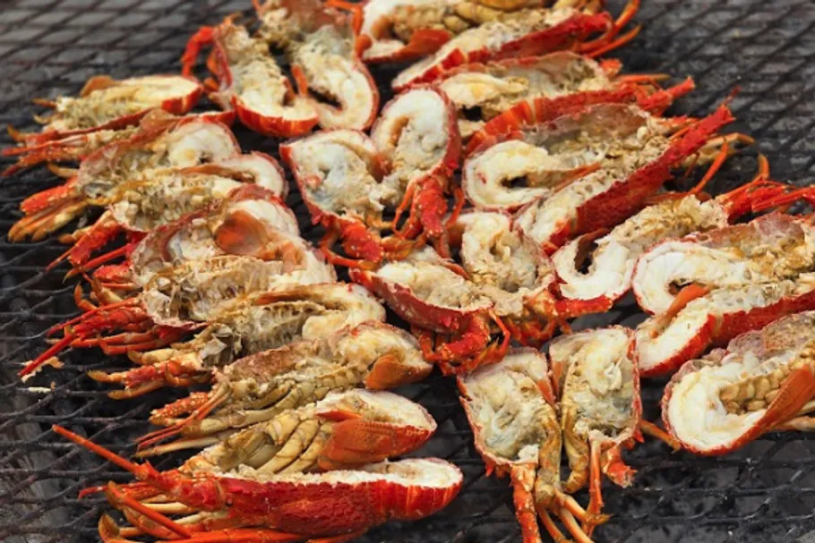 Halved lobsters grilling on metal grid.