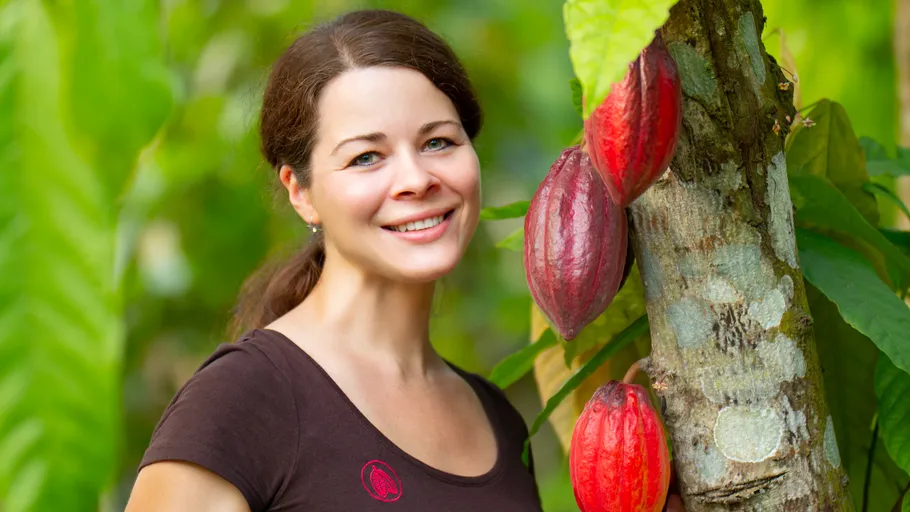 Woman smiling beside cocoa tree in plantation.