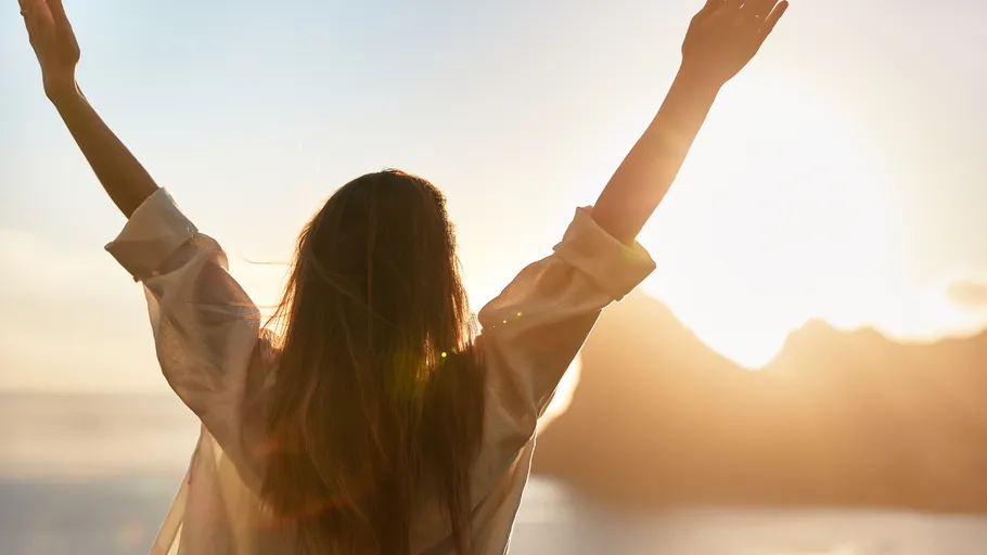 Frau hebt Arme zum Sonnenaufgang im Freien.