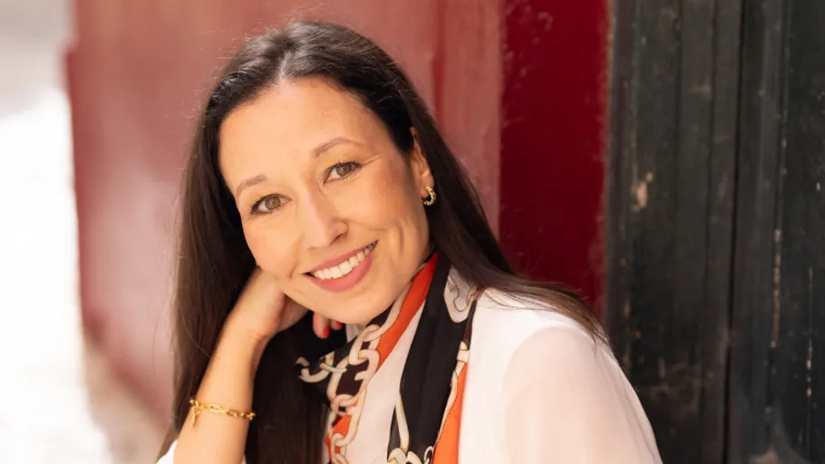 Woman smiling, leaning on hand outdoors.