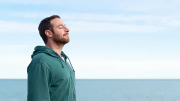 Man in green hoodie breathing by sea.