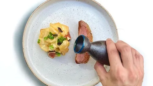 Hand gießt Soße auf Gourmet-Gericht.
