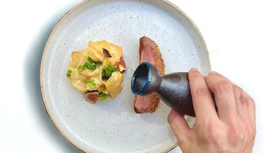 Hand gießt Soße auf Gourmet-Gericht.