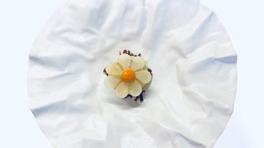 Blumenförmiges Dessert auf zerknittertem weißen Teller.