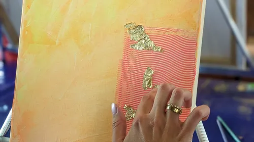 Hand applying gold leaf on abstract painting.