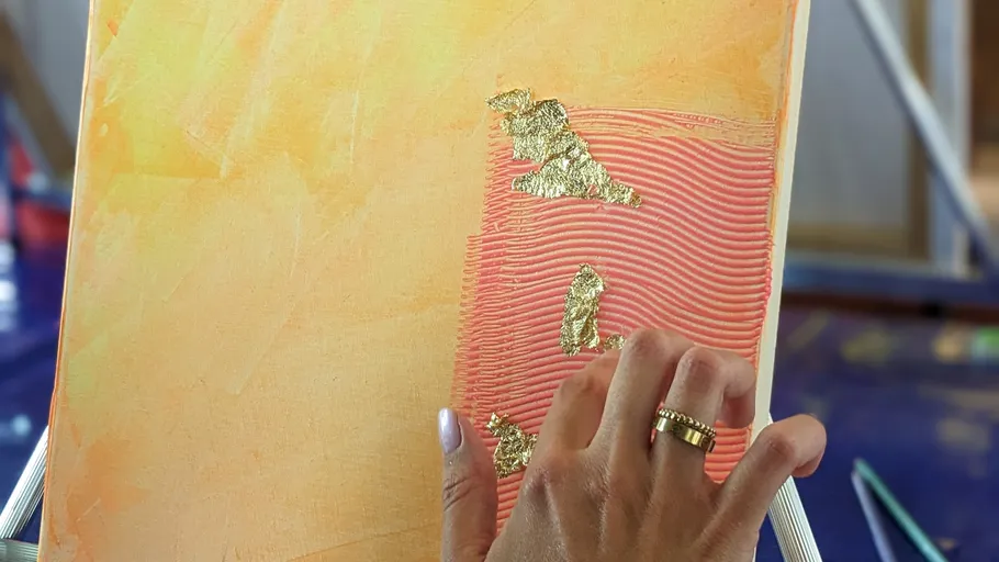 Hand trägt Blattgold auf abstraktes Gemälde auf.