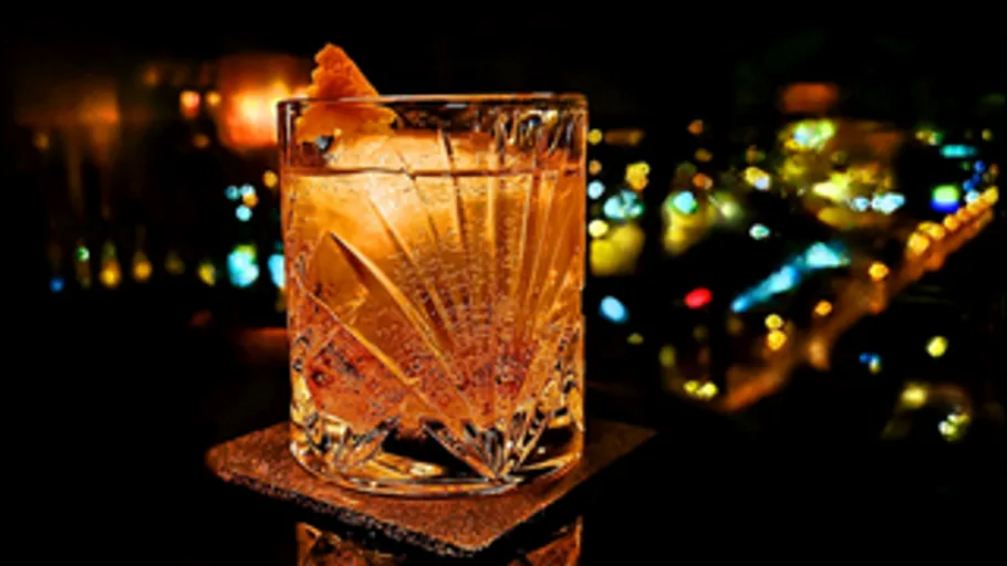 Cocktailglas auf Tisch, Stadtlichter im Hintergrund.