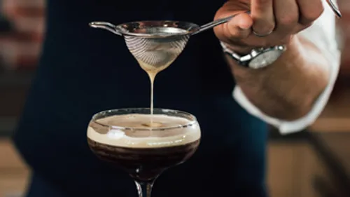 Barkeeper gießt Getränk durch Sieb ins Glas.