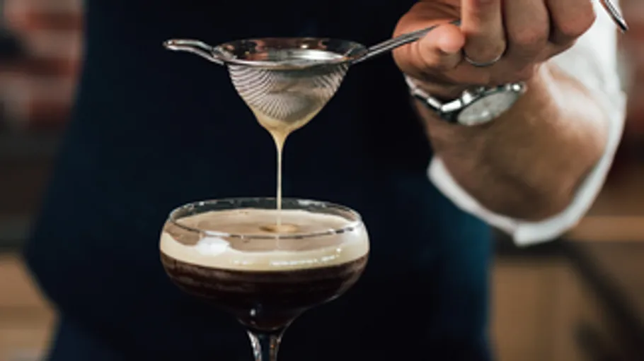 Bartender pouring drink through strainer in glass.