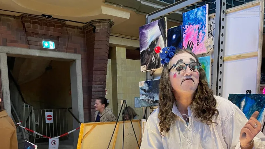 Clown mit Kunstwerken in industriellem Raum.